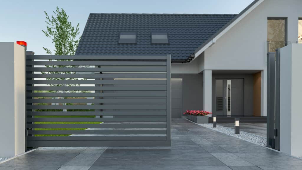 Portail Coulissant Moderne Gris et Maison Contemporaine Portail coulissant moderne gris ouvrant sur l'allée pavée menant à une maison contemporaine au toit sombre.